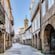 A Gothic steeple standing at the end of a narrow cobblestone walkway lined with Rennaissance architecture